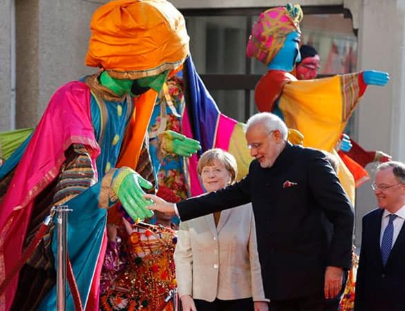 German Chancellor Angela Merkel, center, welcomes India's Prime Minister Narendra Modi, second right, as a traditional Indian music group performs at the opening of the industrial fair in Hanover, Germany, Sunday, April 12, 2015. 