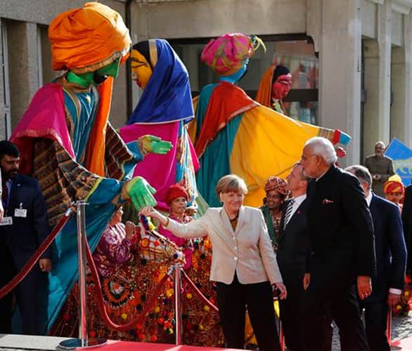 German Chancellor Angela Merkel, center, welcomes India's Prime Minister Narendra Modi, right, as a traditional Indian music group performs at the opening of the industrial fair in Hanover, Germany, Sunday, April 12, 2015.