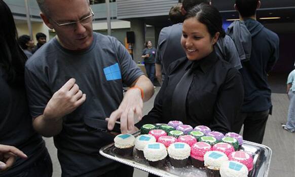 A Microsoft employee reaches for cupcakes being served with the company's logo atop during an event unveiling a new Microsoft Windows operating system.