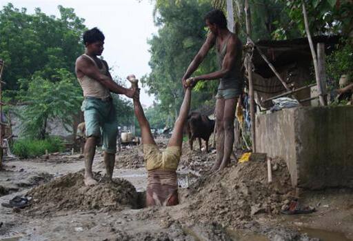 The Cable Guy: Labourers hold their colleague to install underground electric cables on a roadside at Noida.