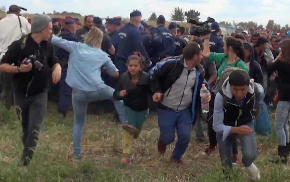 In this image taken from TV a Hungarian camerawoman, center left in blue, kicks out at a young migrant who had just crossed the border from Serbia near Roszke Hungary. The camerawoman has been fired after she was caught on video kicking and tripping migrants entering Hungary across the border with Serbia.