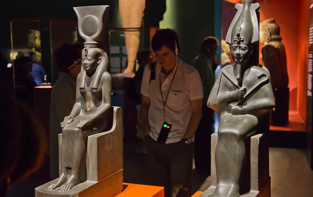 A man stands next to statues of Isis, left and Osiris, Saite period, 26 dynasty, reign of Amasis (570-526 BC), displayed at the Institut du Monde Arabe (Arab World Institute), part of the Osiris, Sunken Mysteries of Egypt exhibition in Paris, France.