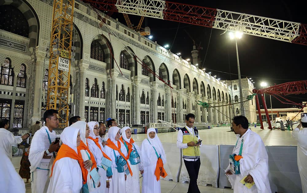 Muslim pilgrims leave the Grand Mosque, as a towering construction crane, top, is seen collapsed over the Grand Mosque, in Mecca, Saudi Arabia.