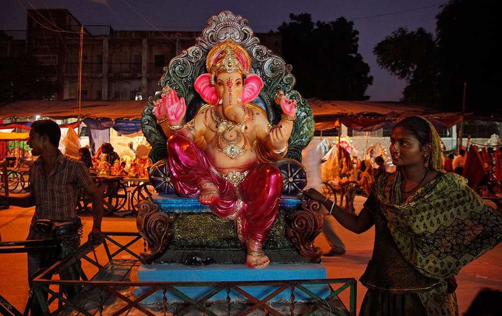 An Indian woman carries an idol of elephant-headed Hindu God Ganesha on a cycle cart for sale on the eve of Ganesh Chaturthi festival in Ahmedabad.