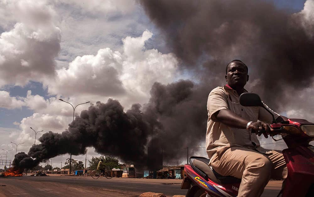 Tires burn, left rear, as people continue protesting against the recent coup in Ouagadougou, Burkina Faso.