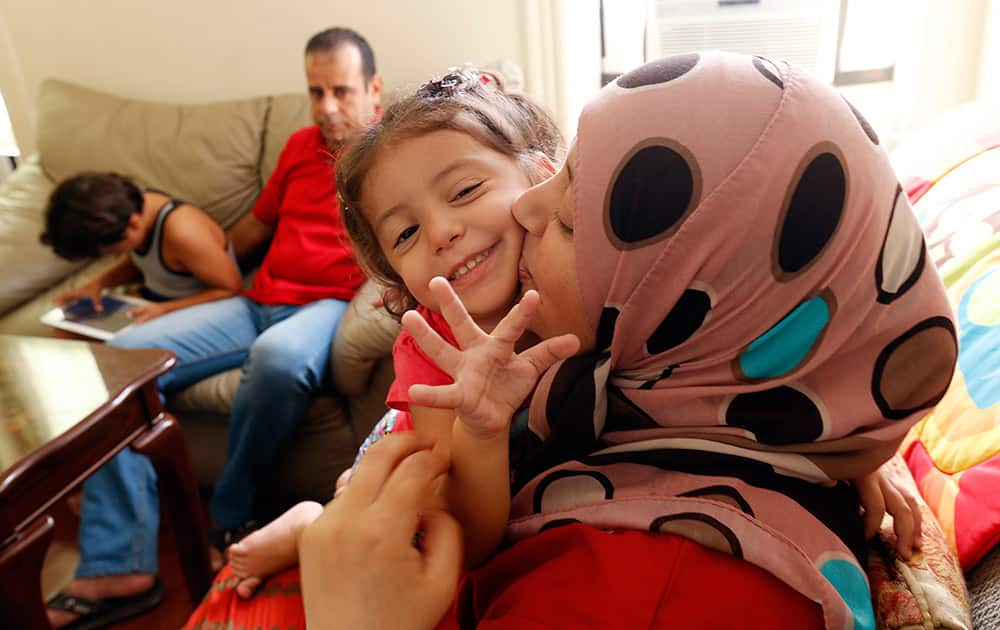 Maaesa Alroustom, center, is kissed by her mother, Suha, as her father, Hussam, back, sits with her brother Wesam in their apartment in Jersey City, N.J.