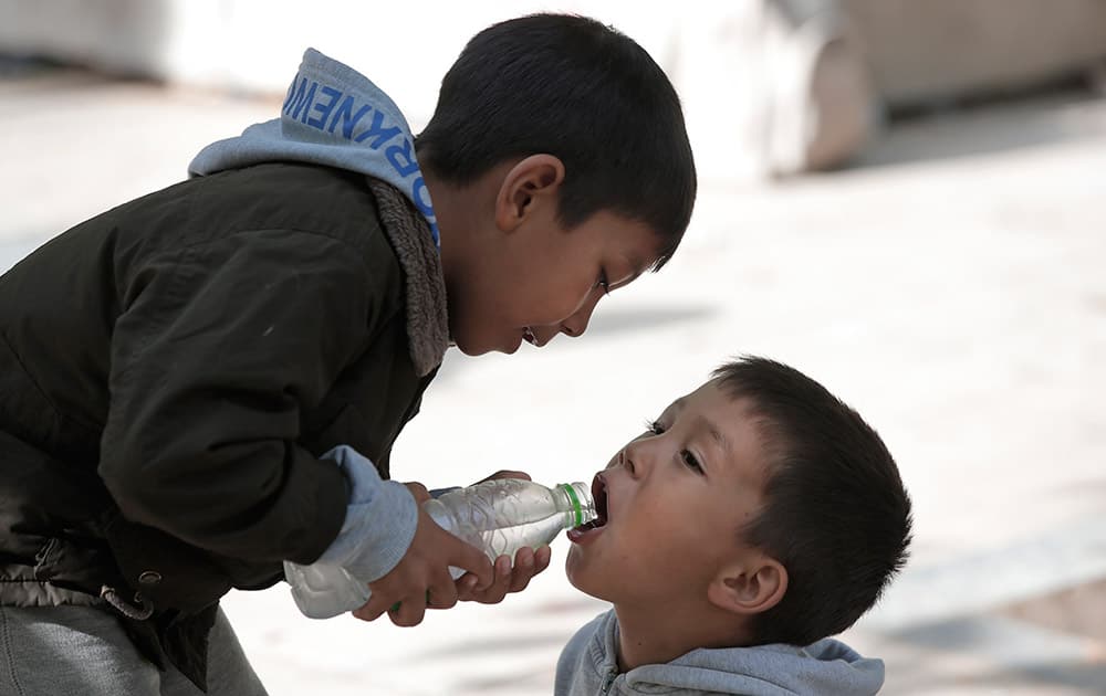 Migrant children share water as they pass time in Victoria square in central Athens.