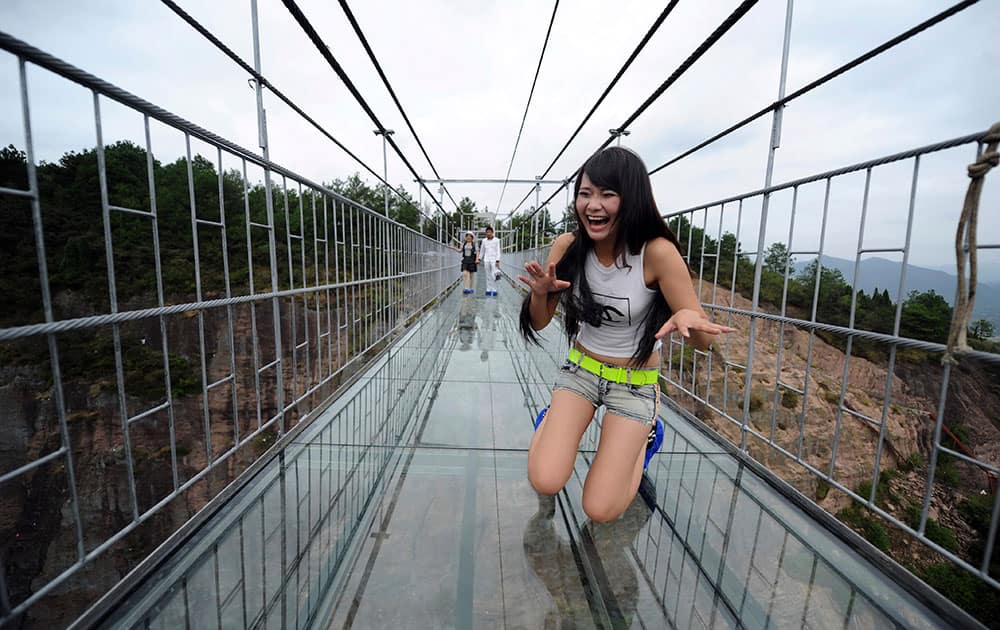 A woman plays around as she walks across a glass-bottomed suspension bridge in a scenic zone in Pingjiang county in southern China's Hunan province. The bridge, 300 meters (984 feet) long and 180 meters (590 feet), opened to visitors on Thursday for the first time since its conversion from a regular suspension bridge was completed.