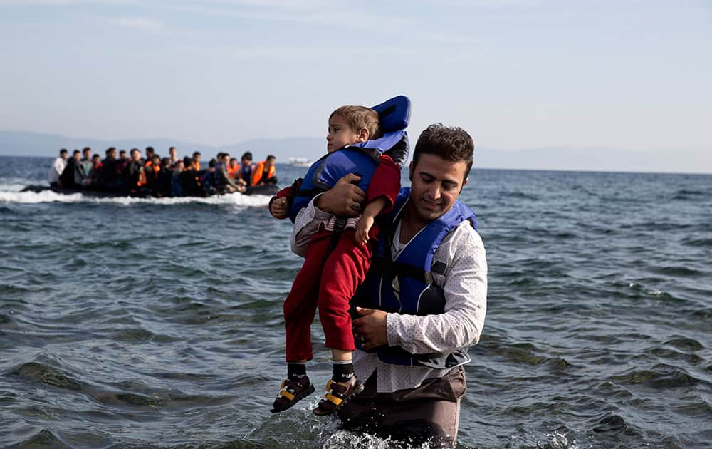 A Syrian refugee carries his child after they arrived from Turkey to the shores of the Greek island of Lesbos, on an inflatable dinghy, with another boat in the background.