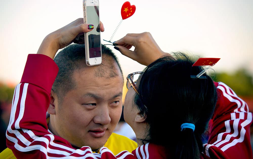 A woman puts a hair clip with the Chinese flag in the shape of heart on a man's head after a flag raising ceremony at Tiananmen Square on National Day, the 66th anniversary of the founding of the People's Republic of China, in Beijing.