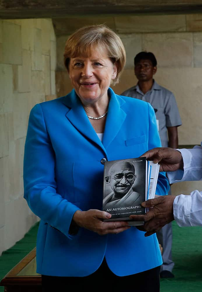 German Chancellor Angela Merkel shows a book of Mahatma Gandhi autobiography, presented to her during her visit to the Mahatma Gandhi memorial, in New Delhi.