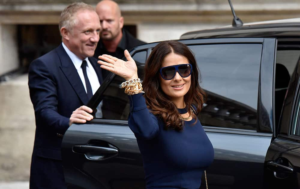 Mexican actress Salma Hayek waves while her husband Francois-Henri Pinault, CEO of luxury group Kering, holds the car door after Stella McCartney's spring-summer 2016 ready-to-wear fashion collection presented during the Paris Fashion Week in Paris, France.