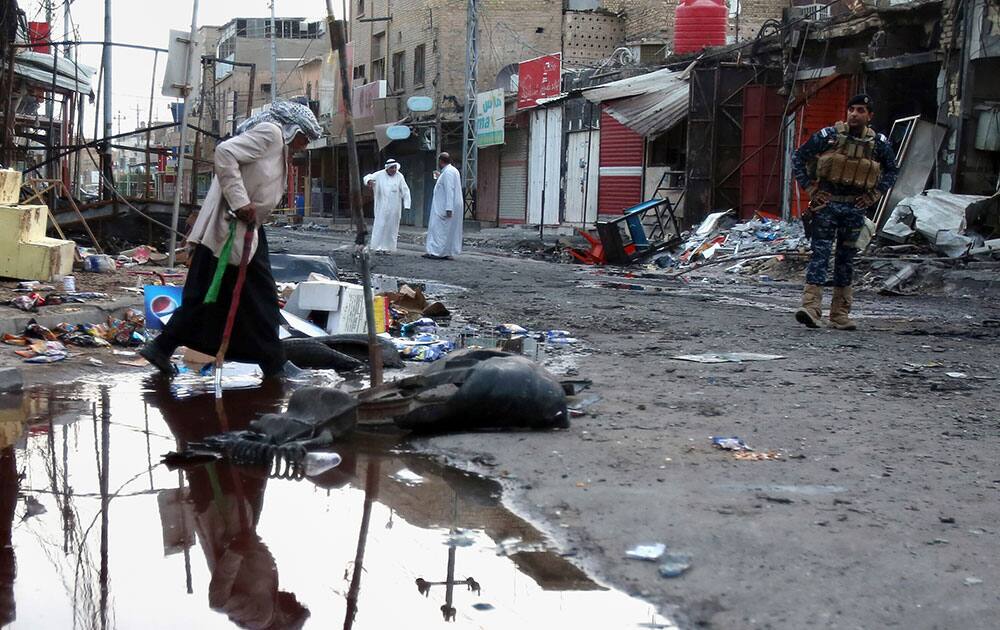 A federal policeman stands guard as civilians inspect the aftermath of a car bomb explosion in a busy commercial district of al-Zubair, a suburb of the predominantly Shiite city of Basra, 340 miles (550 kilometers) southeast of Baghdad, Iraq.