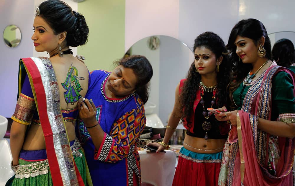 An Indian girl gets a paint tattoo on her back as others watch in preparation of forthcoming Hindu Navratri festival are photographed reflected in a mirror, in Ahmadabad, India.