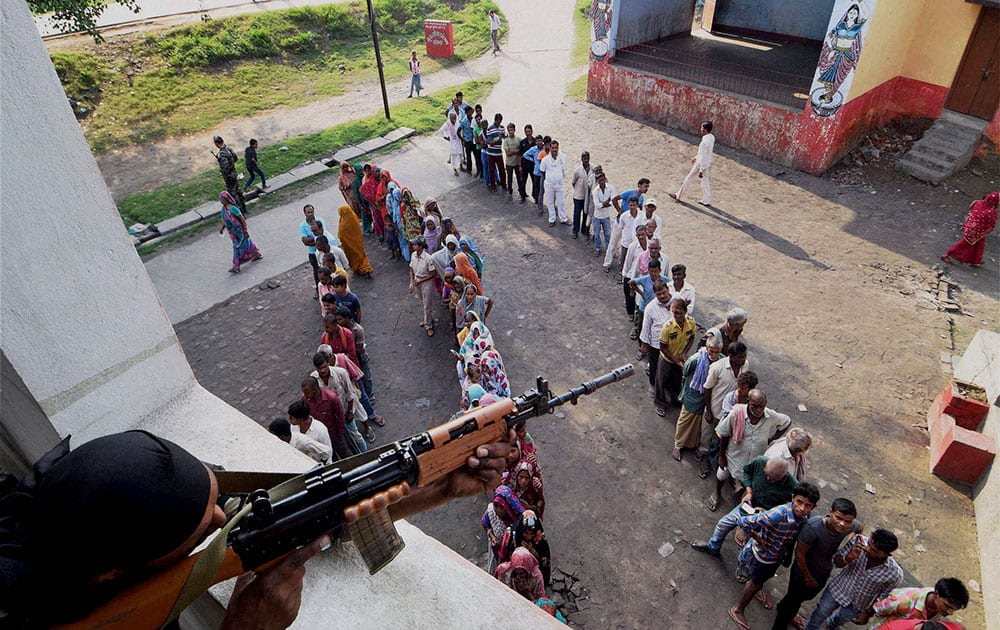 A security person keeps vigil as voters wait in queues to cast votes at a polling station during Bihar assembly elections in Begusarai.