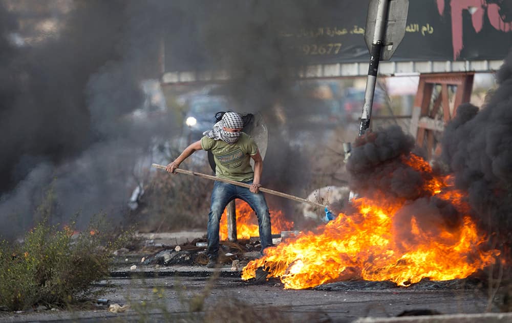 A Palestinian pushes burning tries during clashes with Israeli troops near Ramallah, West Bank.
