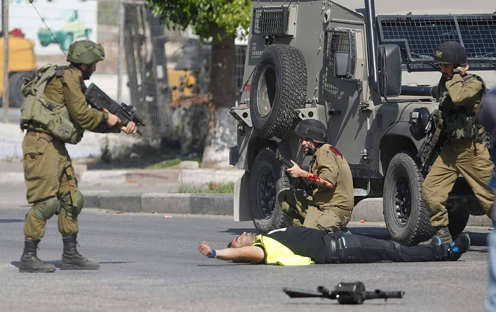 An Israeli soldier shoots a Palestinian holding a knife after he stabbed another Israeli soldier, seen kneeling, during clashes in Hebron, West Bank.