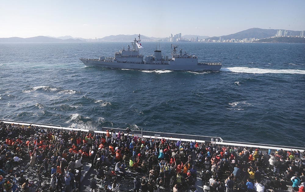 People on the transport ship Dokdo waves as South Korean navy's destroyer Yang Manchun sails by during a media day for a naval fleet review off South Korea's southeastern coast near Busan, South Korea.