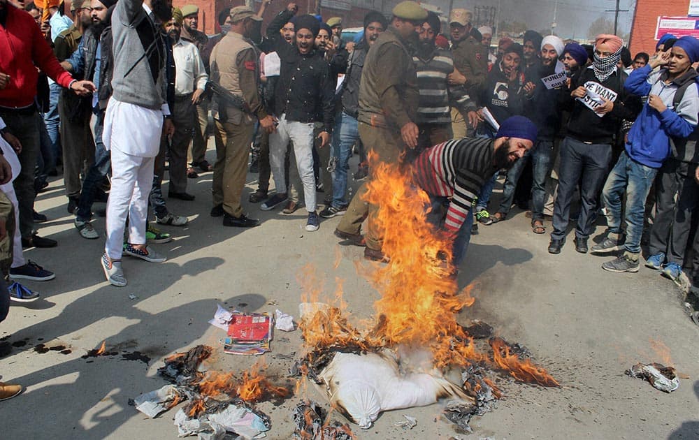 Sikh protesters trampling the burning effigy of Parkash Singh Badal-led government and Gurbachan Singh, as a police officer tries to stop them during their protest against the alleged desecration of religious book and Punjab firing incident, in Srinagar.