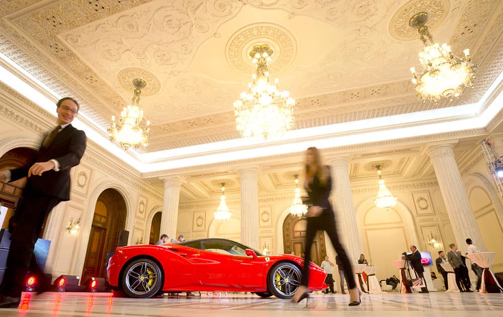 People walk by a Ferrari 488 GTB during the car's launch in Romania inside the Palace of Parliament, formerly House of the People, an administrative building completed during the rule of communist dictator Nicolae Ceausescu, in Bucharest, Romania.