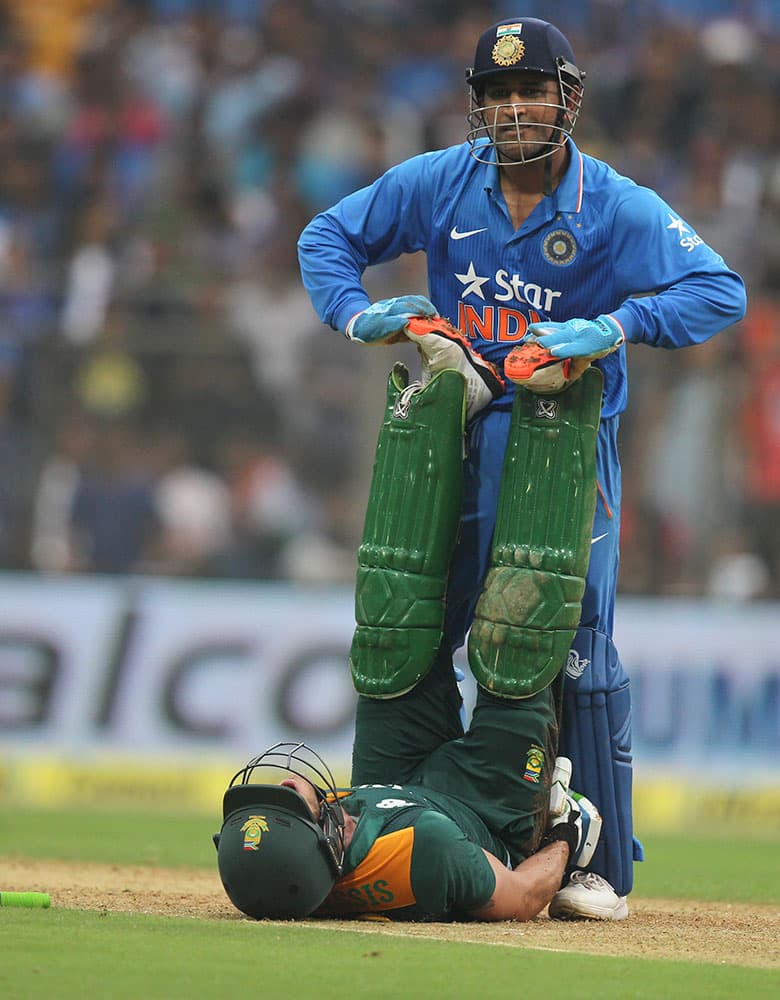 India's captain Mahindra Singh Dhoni, attends to an injured South African batsman Faf du Plessis during the final one-day international cricket match of a five-game series against India in Mumbai, India.