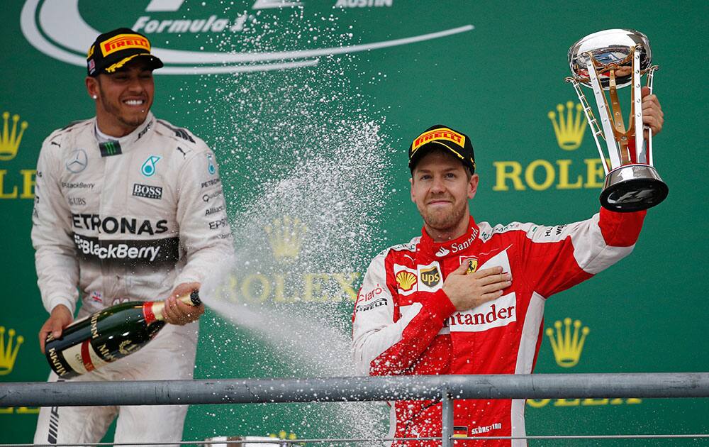 Ferrari driver Sebastian Vettel, right, of Germany, holds his third place trophy as he is sprayed by Mercedes driver Lewis Hamilton, of Britain, following the Formula One U.S. Grand Prix auto race at the Circuit of the Americas in Austin, Texas. 