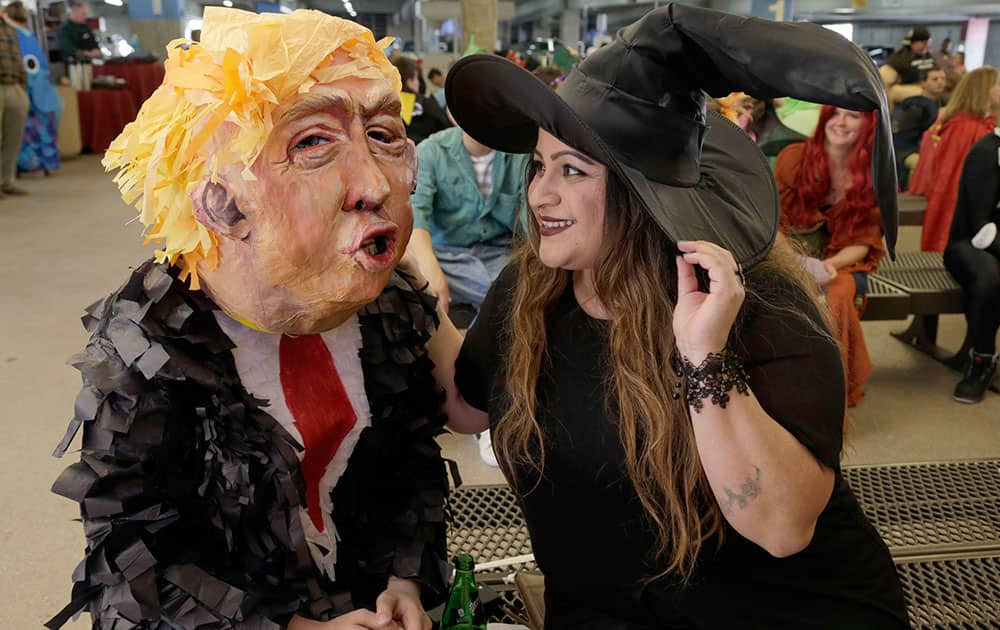 Alia Yusuf, left, wears a 'Donald Trump' mask, with Stephanie Vidal before the taping of a Halloween themed television show at Warner Bros. Studio in Burbank, Calif.