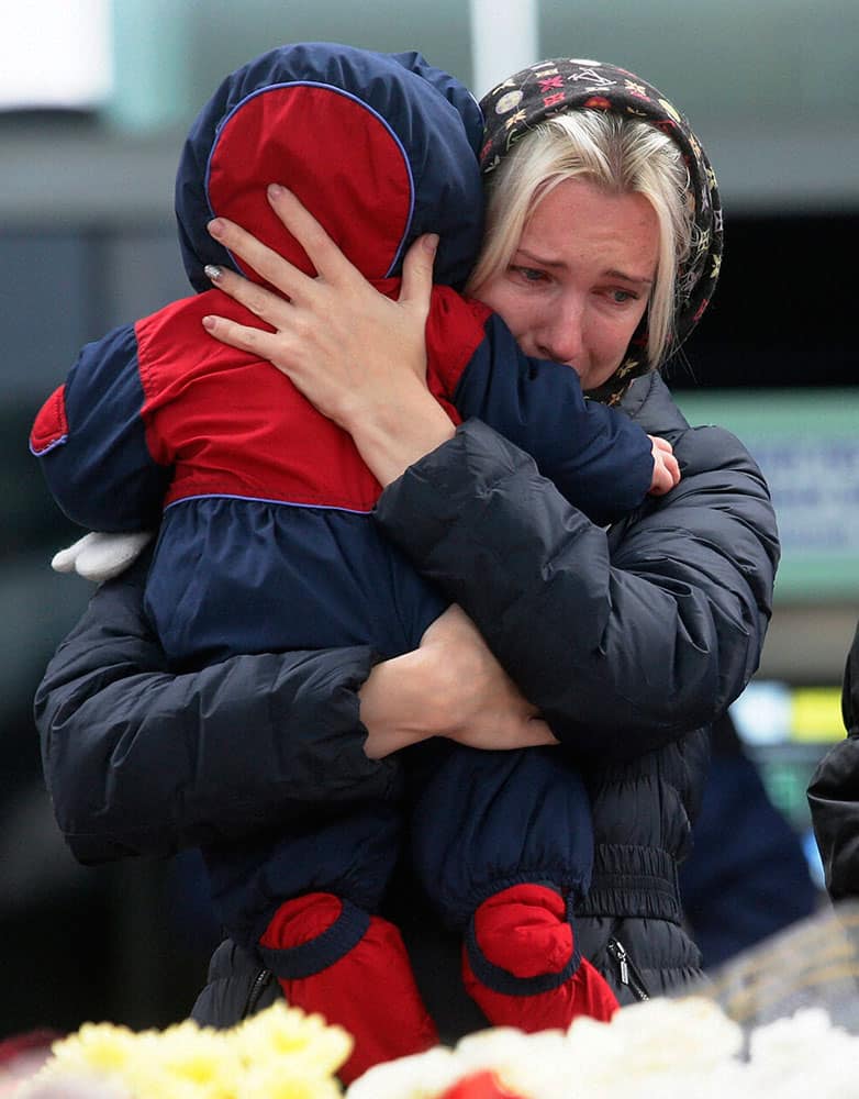 A woman with her baby reacts as she stands near to floral tributes for the victims of a plane crash, at an entrance of Pulkovo airport outside St. Petersburg, Russia.
