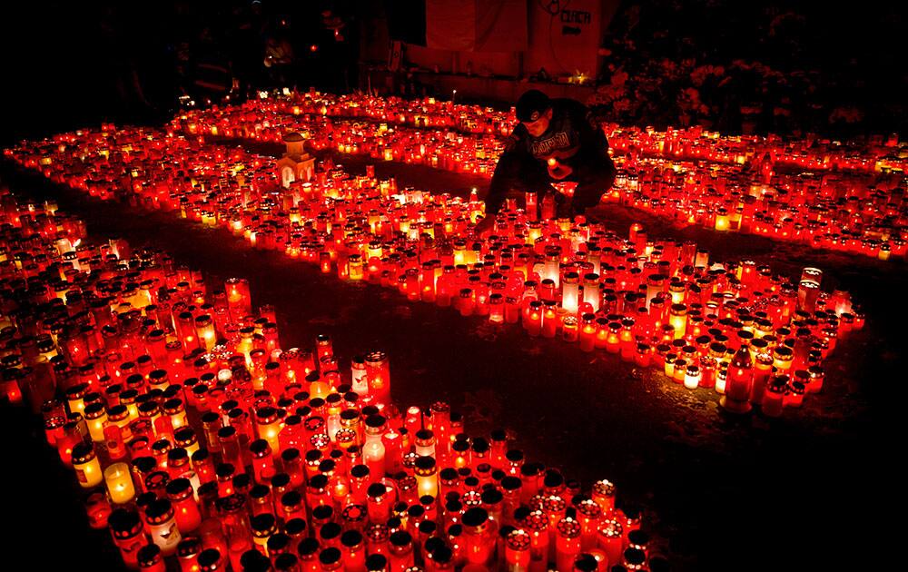 A riot policeman places a candle, collected from people waiting to pay respects to the victims of a fire, outside the Colectiv nightclub, in Bucharest, Romania