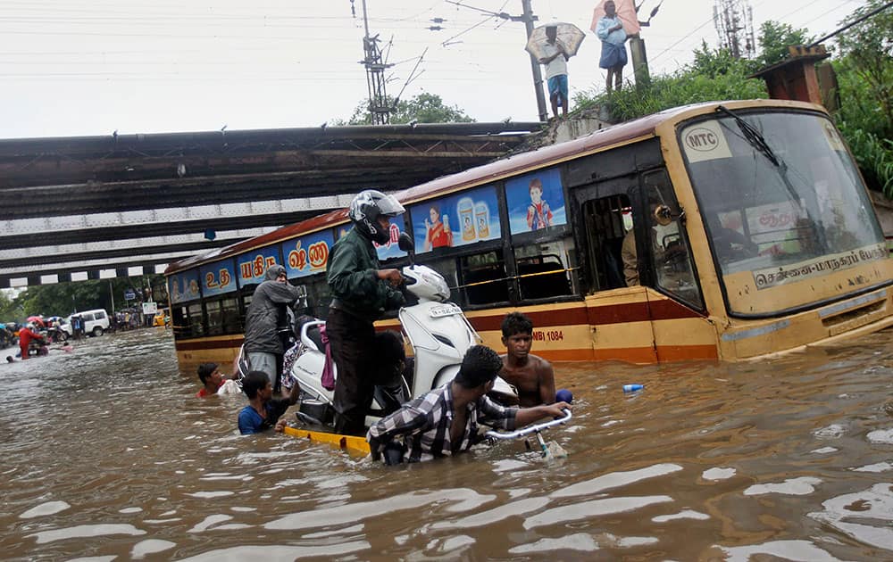 People help a man carry his two-wheeler on a cycle cart as they wade through a waterlogged subway in Chennai.