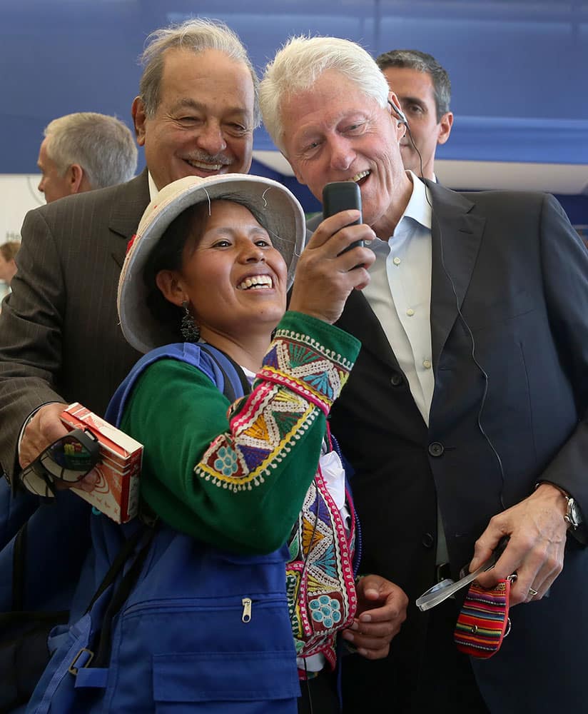 An Andean woman takes a photo of herself with former President Bill Clinton, right, and Mexico's billionaire Carlos Slim, during their visit to the San Juan de Lurigancho district of Lima, Peru.