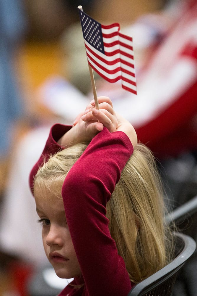 A child holds an American flag over her head during a Veterans Day ceremony in the Countryside YMCA's gymnasium in Lebanon, Ohio.