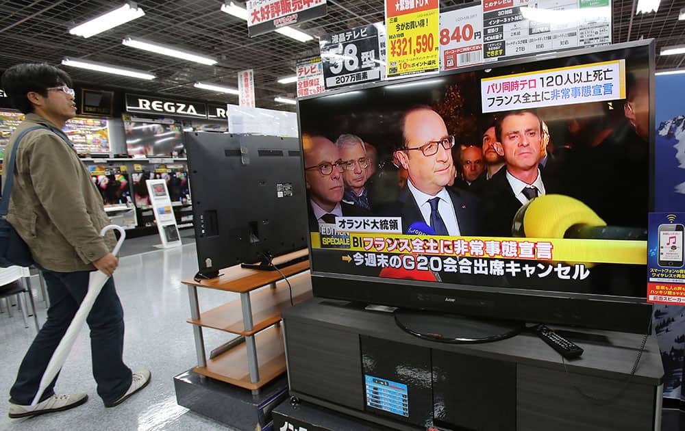 A man walks past a TV screen, which shows French President Francois Hollande speaks about Friday's shootings and explosions in a news program, at Yamada Denki discount store in Tokyo.