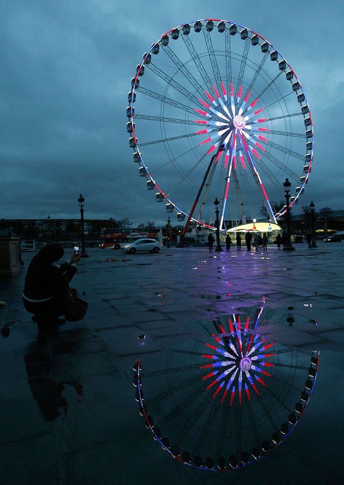 A woman pictures the ferris wheel illuminated with the French colors on the Concorde square in Paris.