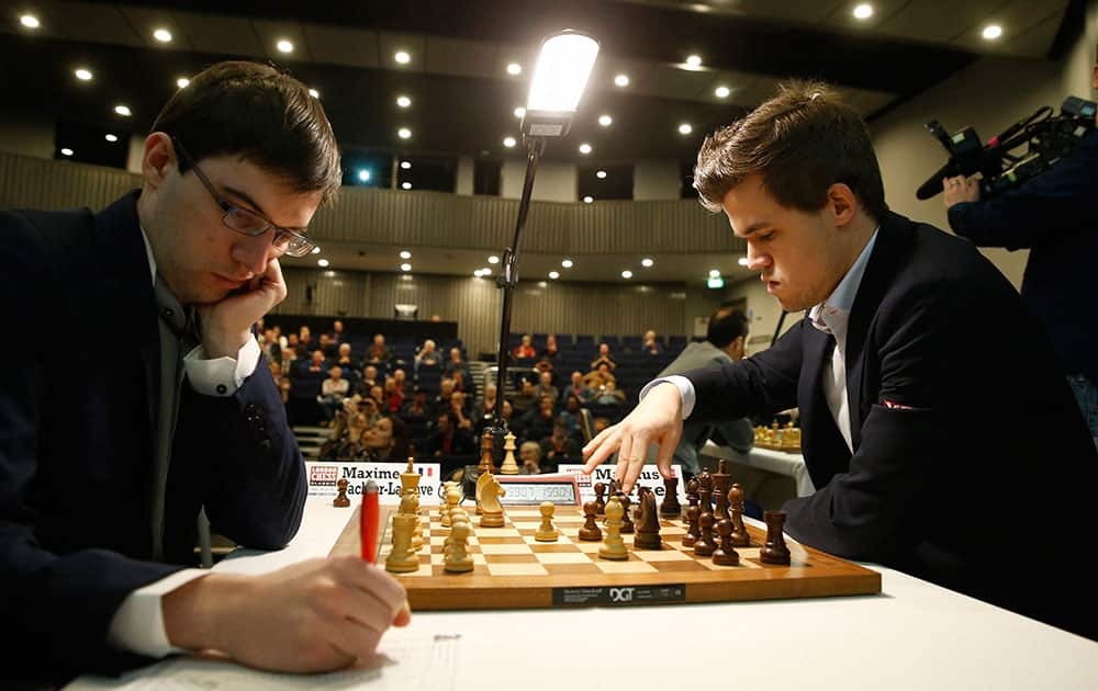 Magnus Carlsen, right, of Norway the current world chess champion and ranked number one in the world, makes a move as he plays against Maxime Vachier-Lagrave of France, who notes his last move, at the start of the London Chess Classic tournament in London.