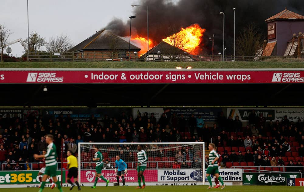 Fire rages at the near by Sixfields Tavern as play continues during the FA Cup second round match between Northampton and Norwich Victoria at Sixfields Stadium, Northampton, central England.