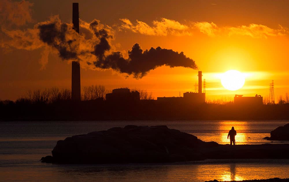 A man photographs the setting sun as powerplant smokestacks battle freezing temperatures in Toronto.