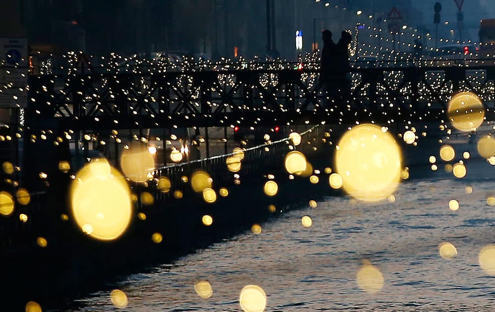People walk on a bridge as Christmas lights illuminate the Darsena dei Navigli, the neighborhood named for the canals that run through this area of Milan, Italy.