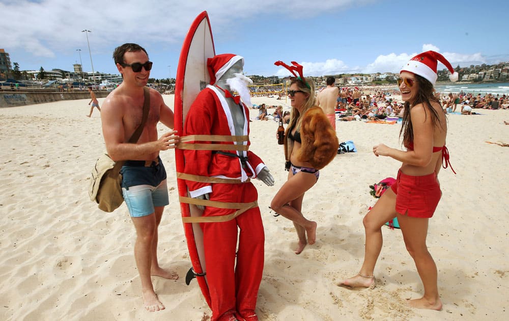 A figure in Santa costume is strapped to a surfboard for easy transport along Bondi Beach as Tom Ray, left, of Britain, Ashley Pronyk of Canada, and Helen Maine, right, of Britain celebrate Christmas Day in Sydney, Australia.