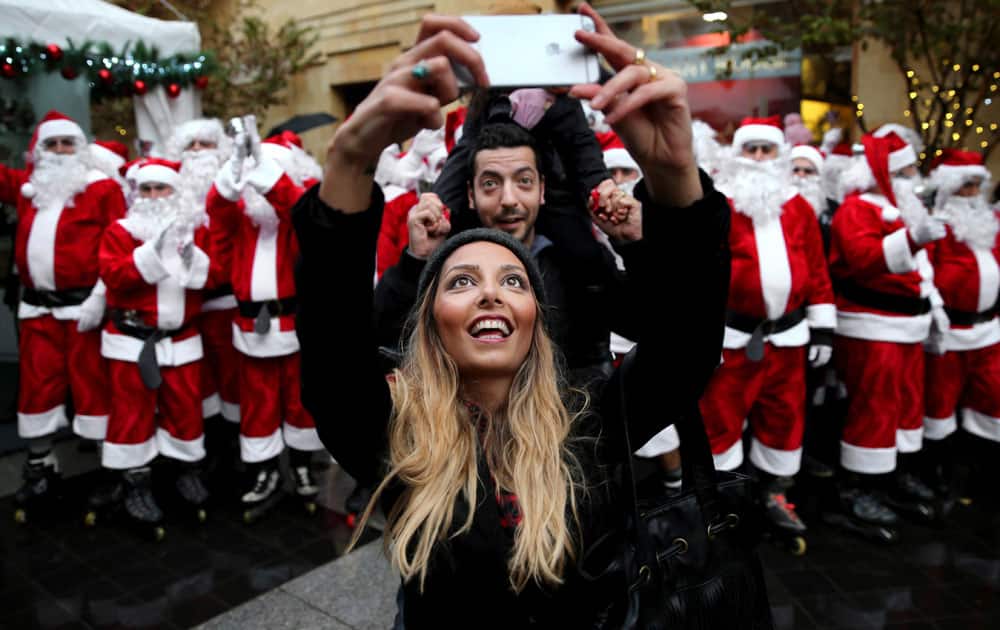 A Lebanese couple take selfie in front men and women wearing Santa Claus costumes during a parade for Christmas, in downtown Beirut, Lebanon. 