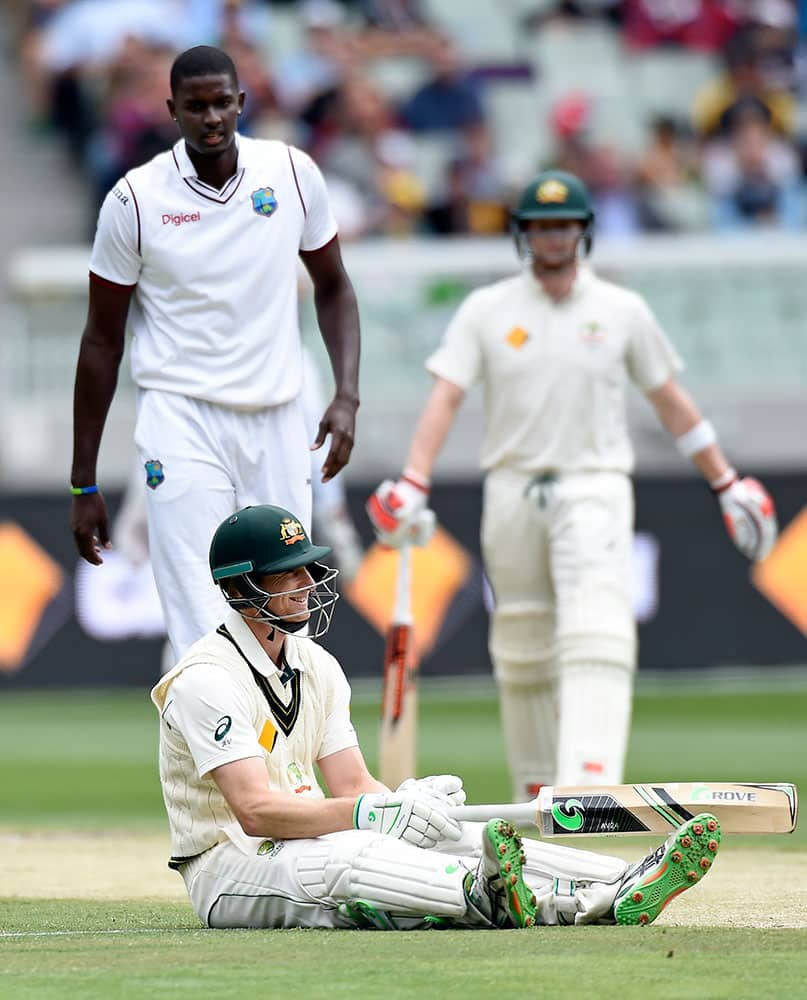 West Indies' Jason Holder, left watches on as Australia's Adam Voges lies on the ground after completing a run during their cricket test match in Melbourne, Australia.