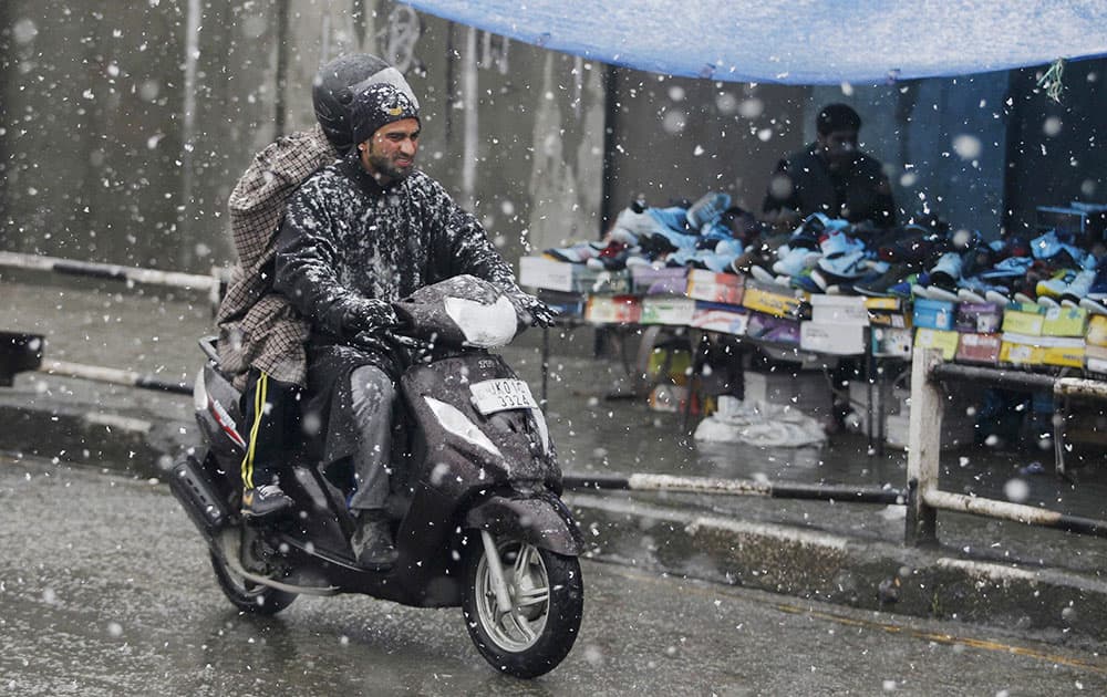 Two men ride a scooter during snowfall in Srinagar.
