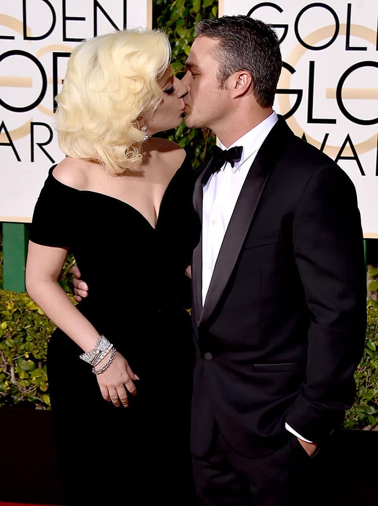 Lady Gaga, left, kisses Taylor Kinney as they arrive at the 73rd annual Golden Globe Awards at the Beverly Hilton Hotel in Beverly Hills, Calif.