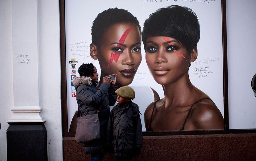 David Bowie style makeup is seen along with fans' tributes drawn onto an ad for his wife Iman's cosmetic range on the side of a store next to where people are laying flowers underneath a mural of him by artist Jimmy C in Brixton, south London.