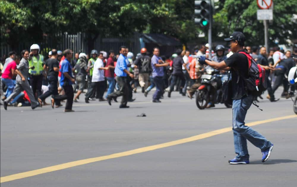 In this photo released by China's Xinhua News Agency, an unidentified man with a gun walks in the street as people run in the background on Thamrin street near Sarinah shopping mall in Jakarta.