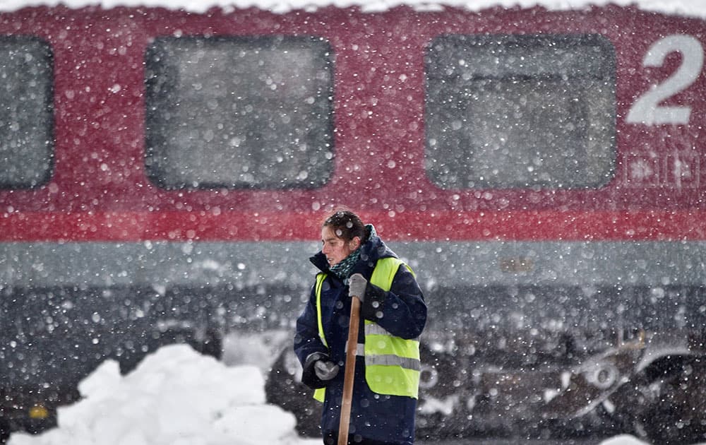 A woman takes a break from clearing snow, back dropped by a delayed train during a blizzard at the Gara de Nord, the main railway station in Bucharest, Romania.