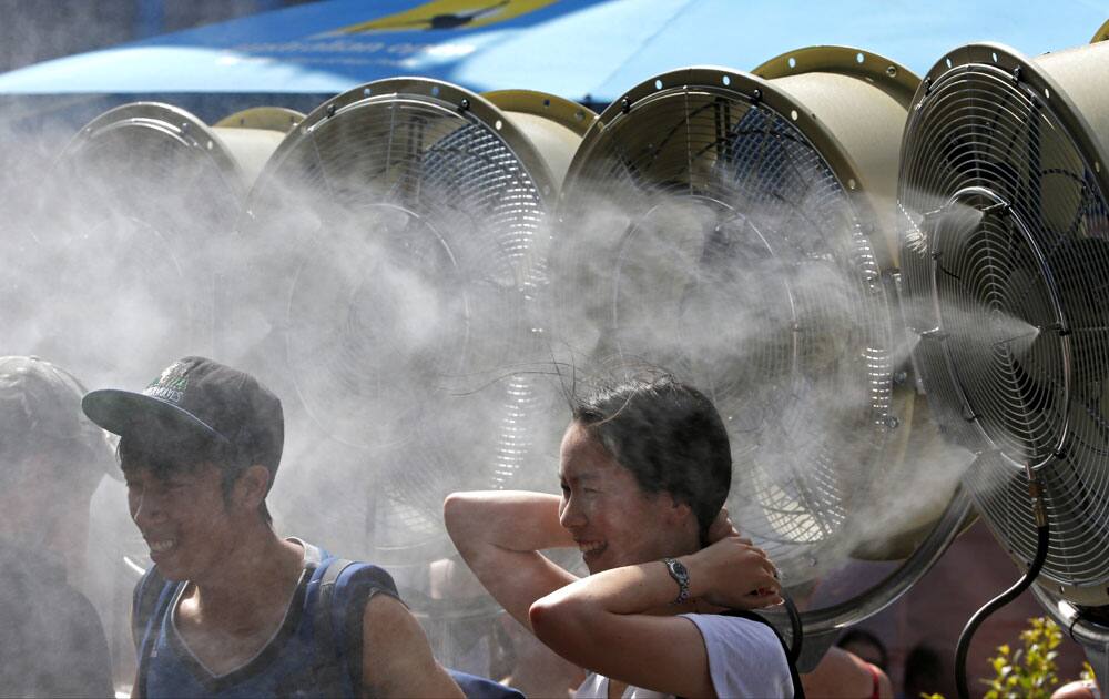 Tennis fans stand before cool water mist to cool down at the Australian Open tennis championship in Melbourne, Australia, Monday, Jan. 18, 2016.
