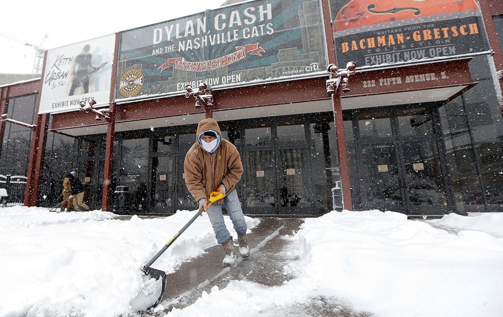 Adrian Lapas scoops snow at the entrance to the Country Music Hall of Fame and Museum, in Nashville, Tenn.