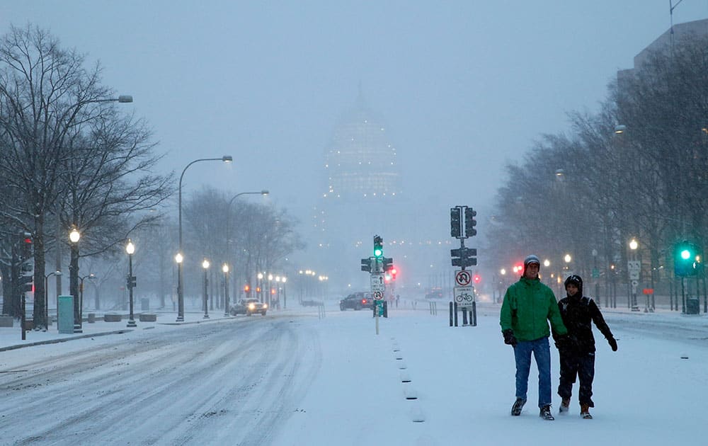 Madison Riley and Katie Lantuh walk down the middle of Pennsylvania Avenue with the US Capitol behind them, as the snow falls, in Washington.