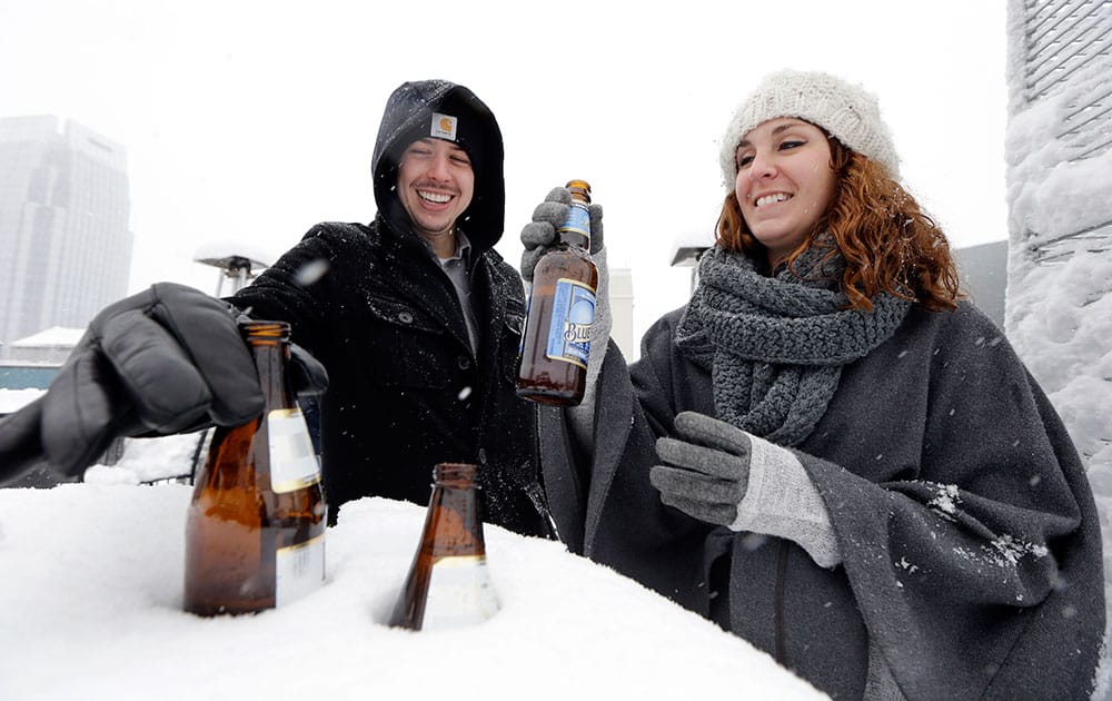 Chris Haltom and Mandy Olsen, both from Dallas, remove their beer from a snow-covered tabletop where they were keeping it cold as they spend the afternoon on a rooftop bar, in Nashville, Tenn.